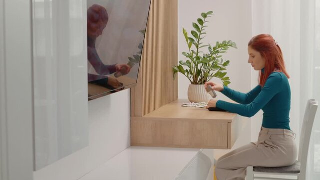 A woman takes out her glucometer and prepares to test her blood sugar level at home. This happens in a simple room with a plant and a table.