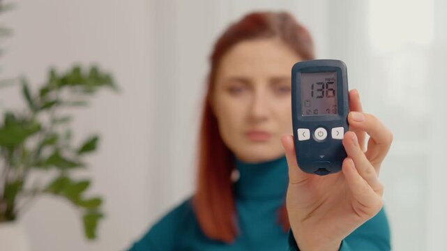 A woman holds a glucometer that shows a reading of 136 mg dL. This indicates high blood sugar levels. She discusses what this means for her health.