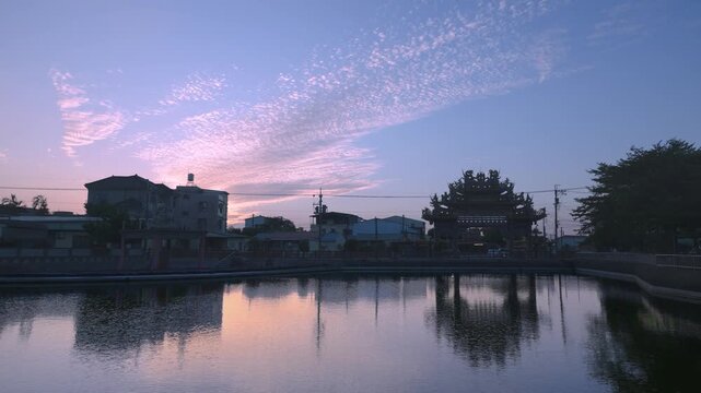 A serene twilight scene in Shanhua, Tainan, Taiwan, featuring a traditional temple gate beautifully reflected in a calm pond. The sky is painted with soft pink and purple clouds.