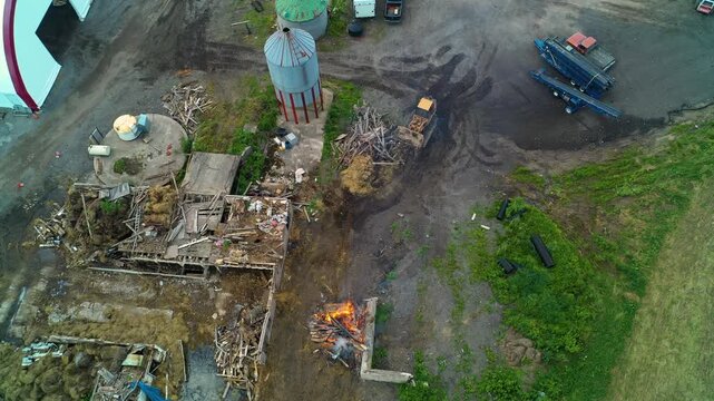 Aerial view of construction site on a farmyard with debris piles, fire and greenery surroundings.
