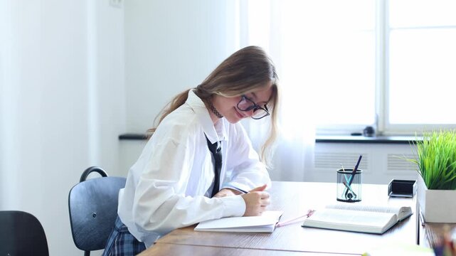 A focused student in glasses and a white blouse studies at her desk, switching between pens while surrounded by books and greenery near a bright window.