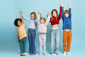 Obraz premium Diverse excited children standing together with raised hands on a blue background