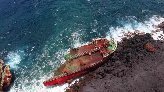 Drone orbit and ascent around stranded tanker on volcanic lava coast, Chemin des Laves, Reunion Island
