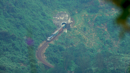 Fototapeta premium AERIAL: Long freight train comes out of the tunnel and moves through the forest.