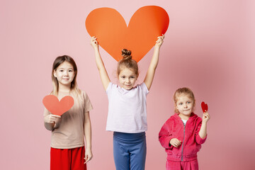 Three diverse children showing paper hearts for love, friendship, and charitable giving
