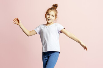 Happy little girl raising hands expressing joy and fun on pink background