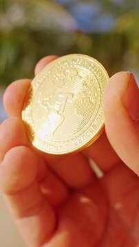 Vertical video. A Hand Holds a Gold Tether USDT Token Over a Sunlit Tropical Beach Highlighting Stable Digital Currency and Modern Blockchain Finance