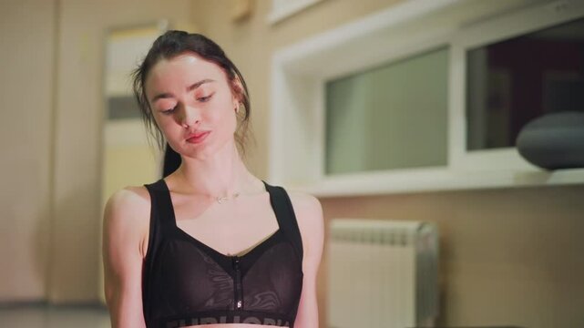 Woman performing core workout at home in small studio with black sports bra and pink stability ball, slow controlled reps and steady breathing, focused expression, warm evening light, toned midline