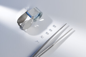 Magnifying loupe and tweezers with loose diamonds on white background