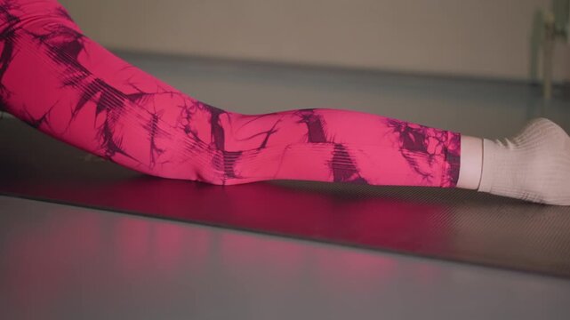 white woman doing leg split on mat in studio with pink patterned leggings and socks, toes pointed, hamstring tension, precision alignment, focused training atmosphere and disciplined mobility practice