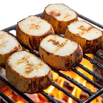Sliced grilled yac?n root vegetables are cooking over a charcoal fire on a barbecue grill with visible flames creating a close up view of this tasty food item.