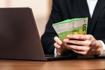 Businessman holding euro banknotes at a desk with a laptop in a modern office, focused on financial transactions. Concept business, finance, office work