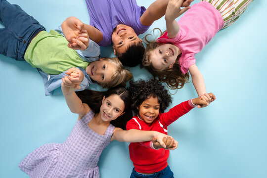Portrait of positive diverse multinational kids lying in circle looking at camera on blue background