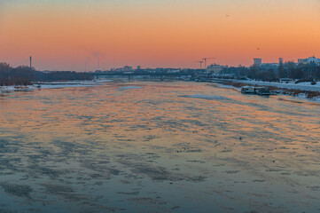 Widok z Mostu Gdańskiego na rzekę Wisłępo kt&oacute;rej płynie  kra lodowa o zachodzie słońca.