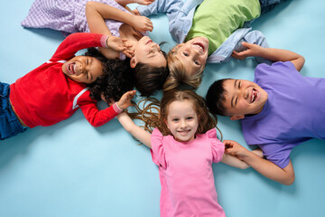 Portrait of happy multinational children laughing lying in circle looking at camera fooling around