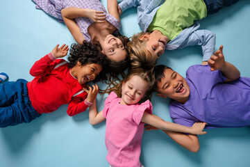 Portrait of happy multinational children laughing lying in circle looking at camera fooling around