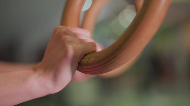 closeup hands gripping wooden ring, steady tension and wrist engagement, shallow depth of field with gym bokeh, training warmup focusing on grip strength and control, coach demonstration vibe