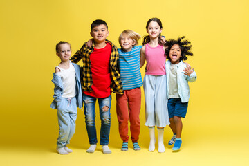 Obraz premium Group of happy multinational kids, happy boys and girls hugging together on yellow background