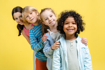 Obraz premium Smiling positive diverse group of happy multinational children posing on yellow background