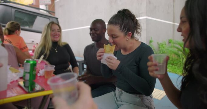 Group of friends sharing pastel Brazilian street food and drinks at outdoor caf&eacute; table expressing joy friendship social bonding casual leisure community togetherness