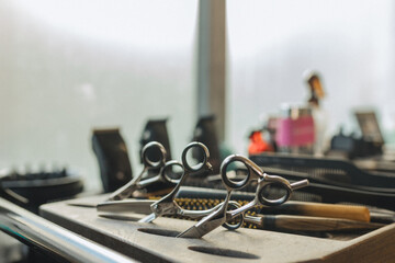 Professional barber scissors and grooming tools on workstation in modern barbershop. Close up of hairstyling equipment, selective focus, male grooming concept, salon atmosphere.