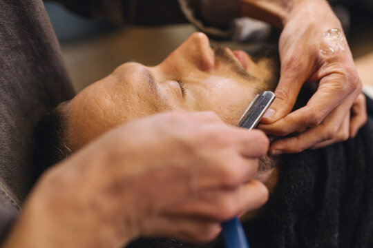 Close up of professional barber shaving male neck with straight razor in barbershop. Beard contouring, classic wet shave, men grooming service and barber work process concept.