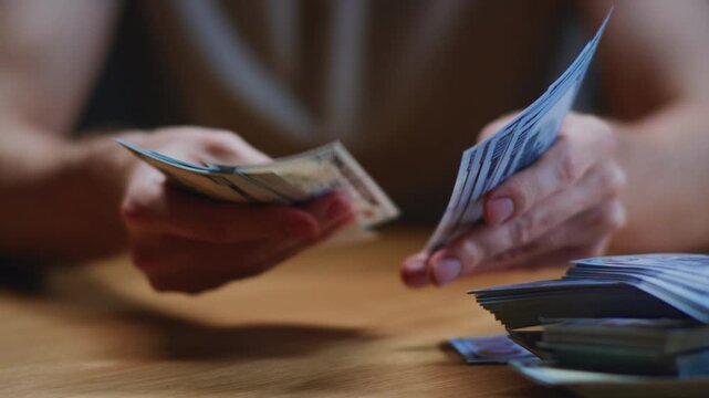 Close up: man trader or businessman counts salary usd banknotes at home with his hands. Male entrepreneur holds stack of dollar bills in palms, keeps money records for budget. Counting american paper
