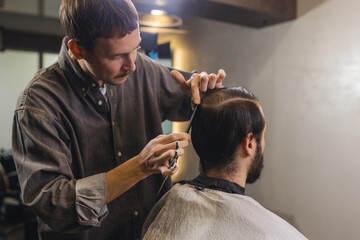 Barber cutting male client hair with scissors and comb. Close up of professional haircut process, precision technique, men grooming service in modern barbershop.