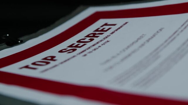 A paper folder of documents with a Top Secret cover page is handled under subdued lighting. Suggestive of spying, espionage, or cover-up.