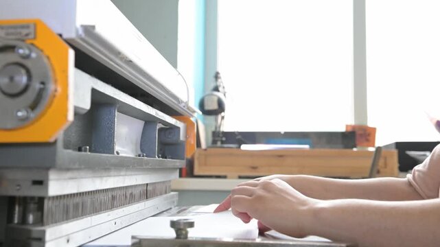 Women's hands in the printing house work at the machine, making holes in the paper to insert the spring for the notebook. Production of calendars and brochures
