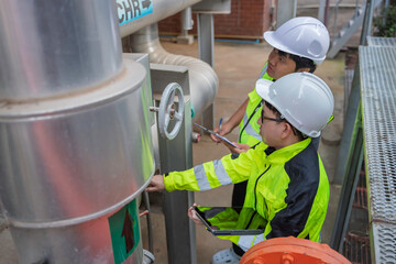 Two Asian engineers inspecting industrial cooling system valves. Professional technicians use a digital tablet for maintenance checks of thermal control equipment at a manufacturing plant.