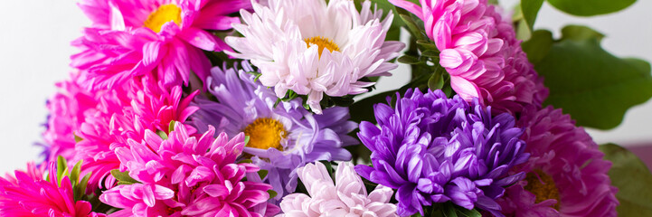 Fototapeta premium A group of flowers in shades of pink, purple, and white are gathered in a vase. The vase rests on a table. The setting is bright and shows the flowers clearly, banner