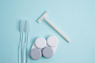 Daily personal hygiene set: white toothbrushes, razor and contact lens cases on blue background