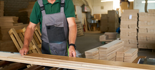A worker in a woodworking plant uses a planer to produce parquet boards.