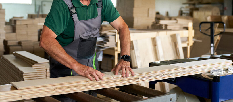 A worker in a woodworking plant uses a planer to produce parquet boards.