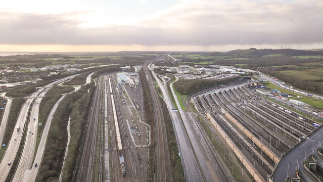 Aerial view of the Ashford Road, a tapestry of roads and railways under a muted sky, where the steel of tracks meets the asphalt, Folkestone, England, United Kingdom.