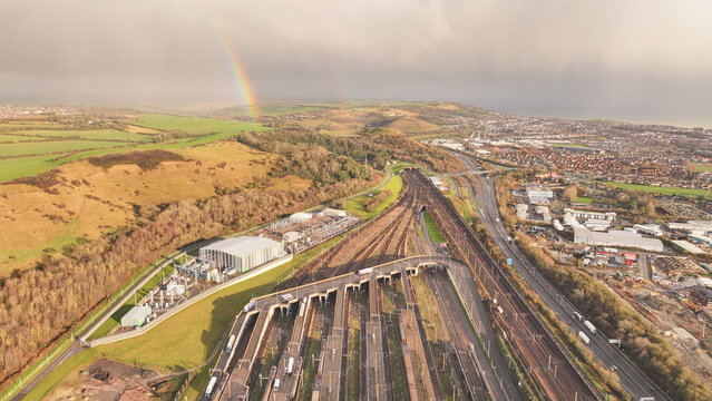 Aerial view of the Ashford Road intersection with a rainbow over the lush green hills contrasting with the urban sprawl, Folkestone, England, United Kingdom.