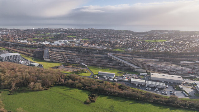 Aerial view of Ashford Road train tracks glinting under the diffused sunlight, contrasting with the lush green fields and dense woodland, Folkestone, England, United Kingdom.