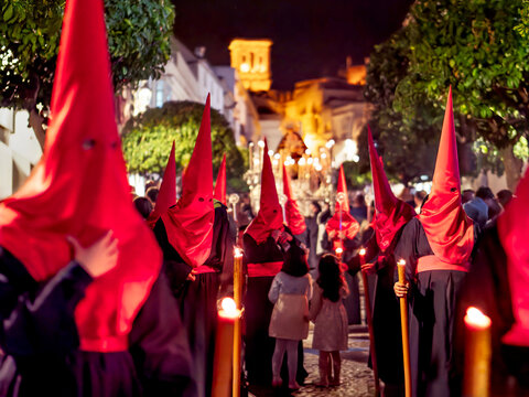 Many nazarenos with red hoods walking in procession