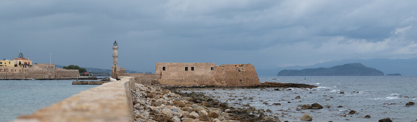 Venetian lighthouse and harbor walls under stormy sky in Chania, Crete