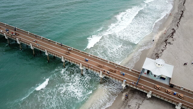 Aerial view of the Juno Beach Pier stretching into the turquoise ocean, contrasting against the sandy shore, Juno Beach, Florida, United States.