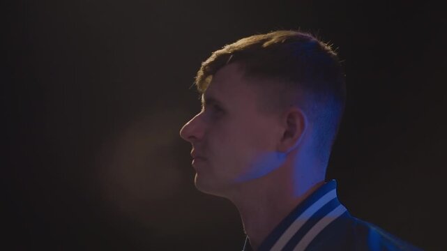 young caucasian man looking upward under lamplight, varsity jacket catching bluish glow, passenger turned observer, traveler plotting next move, dreamer scanning skyline, expression soft with resolve,