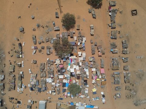 Aerial view of a cluster of tightly packed dwellings under the African sun, casting long shadows on the arid land, Dodji, Louga Region, Senegal.