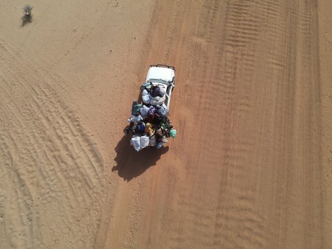 Aerial view of a white vehicle heavily laden with goods traverses the arid landscape, its cargo a colorful contrast against the sandy terrain, Dodji, Senegal.
