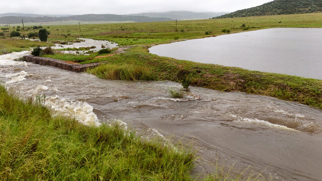 Aerial view of swift waters carve through the verdant landscape, merging into a serene dam under a muted sky, Vaalwater, Limpopo, South Africa.