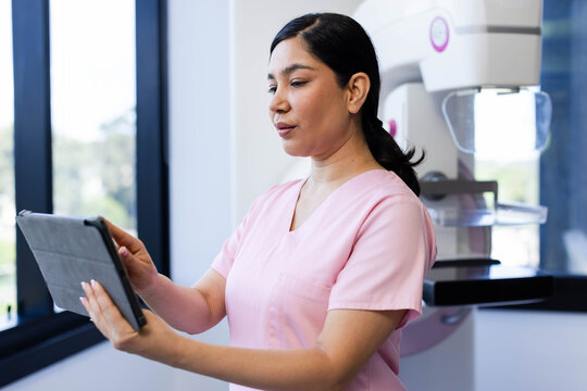 Female medical worker standing in clinic wearing pink scrubs holding tablet, reviewing mammography
