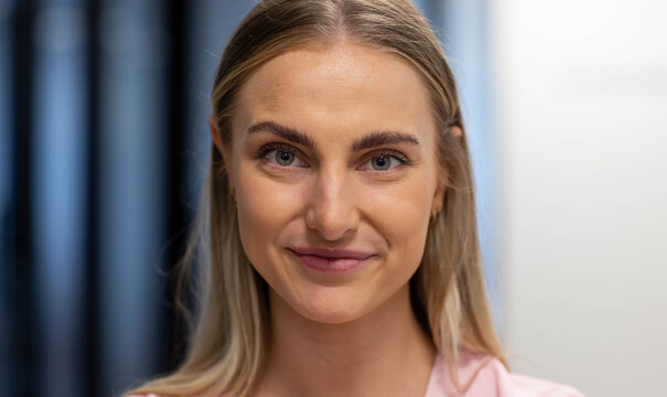 Woman facing camera maintaining eye contact in studio wearing pink blouse gold-hoop on left ear