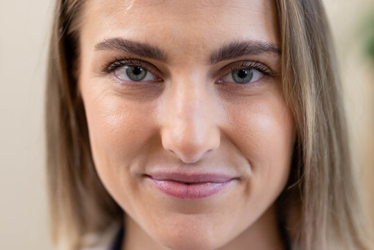 Smiling subtly, woman facing camera in closeup portrait at neutral interior with foliage