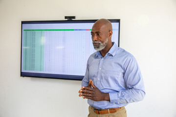 Naklejka premium Senior African American man in shirt showing spreadsheet with webcam in meeting room, copy space