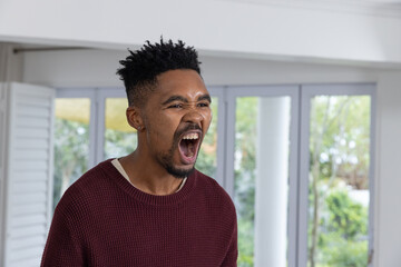 Naklejka premium African American man standing in bright living room near glass doors, shouting and wearing sweater